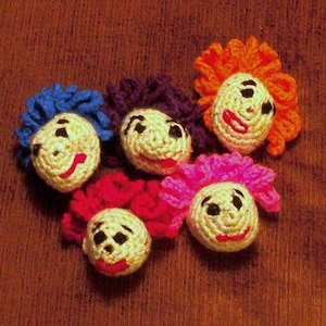 May include: Five crocheted dolls with different colored hair and smiling faces. The dolls are made of yarn and have embroidered features.