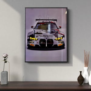 May include: Framed print of a white and black race car with the text "AL MANAR RACING". The car has yellow headlights and a black spoiler. The image is displayed on a wall.