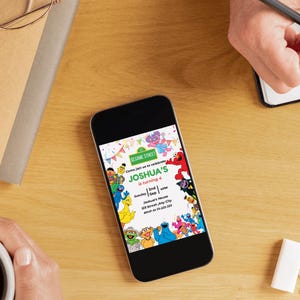 Pu&ograve; includere: Uno smartphone mostra un colorato invito di compleanno di Sesame Street. L'invito recita "Joshua's is turning 4". Il telefono &egrave; su una superficie di legno. Una mano tiene una matita e l'altra una tazza.