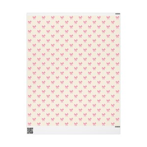 Può includere: Uno sfondo color crema è ricoperto da un motivo ripetuto di piccoli fiocchi rosa. I fiocchi sono uniformemente distanziati e creano un design delicato e femminile. L'immagine è un primo piano di un tessuto o carta stampata.