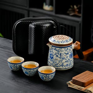 May include: A blue and white floral patterned tea set, including a teapot, three teacups, and a black carrying case. The teapot has a brown handle and lid. The teacups are filled with tea. A wooden coaster is also present.
