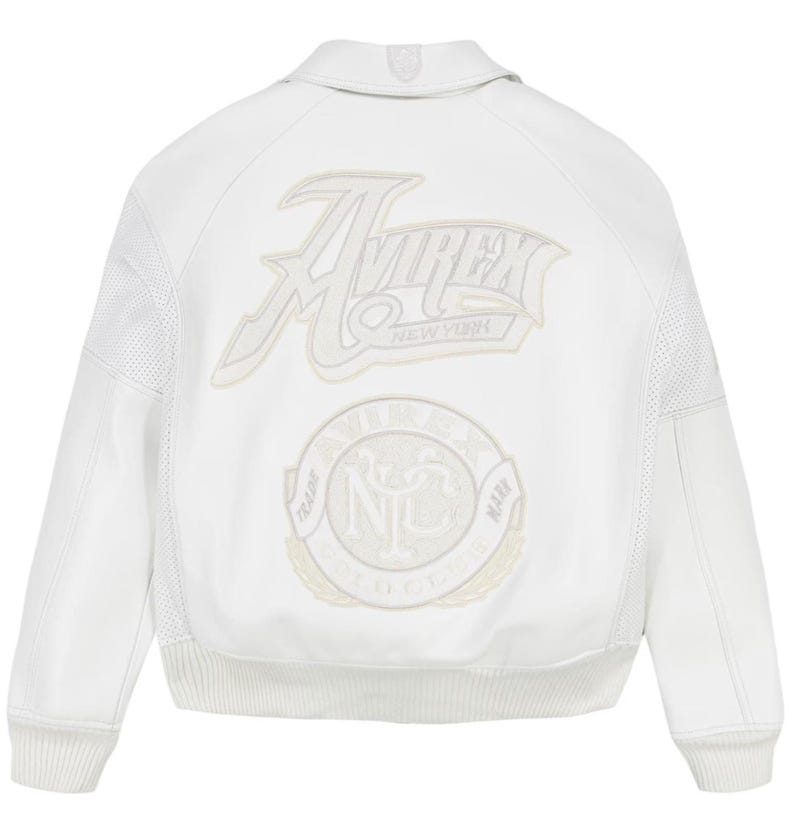 Puede incluir: Chaqueta de cuero blanca con el logo "Avirex New York" y un emblema circular en la espalda. La chaqueta tiene dobladillo y pu&ntilde;os de canal&eacute;, cuello y paneles perforados en las mangas.