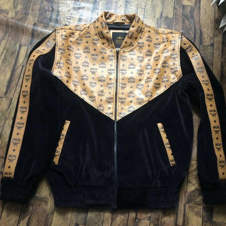 May include: Black and tan zip-up jacket with a repeating logo pattern. The jacket features a tan collar and shoulder yoke, with matching stripes down the sleeves. The body of the jacket is black.