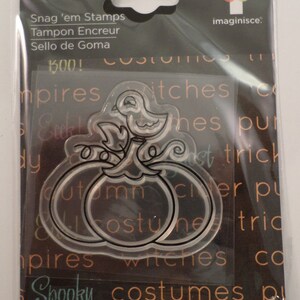 May include: Clear stamp sheet with two pumpkins and a bird on a vine. The stamp sheet is packaged in a clear plastic sleeve with the text "Snag 'em Stamps", "Tampon Encreur", "Sello de Goma", "BOO!" and "imaginisce." printed on the front.