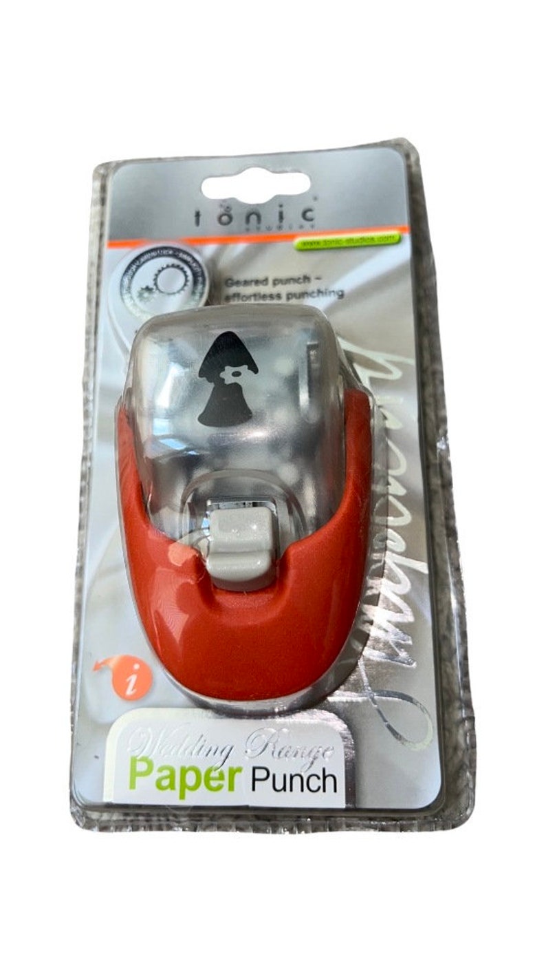 K&ouml;nnte beinhalten: Ein roter und transparenter Papier-Locher aus Kunststoff mit einem silbernen Hebel. Der Locher ist glockenf&ouml;rmig und tr&auml;gt ein Etikett mit der Aufschrift "Wedding Range Paper Punch". Der Locher befindet sich in einer transparenten Plastikverpackung.