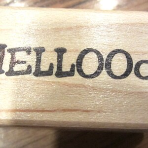May include: A wooden stamp with the word "HELLOOO" printed in black ink.