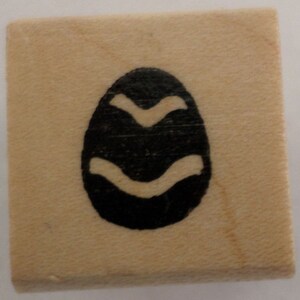 May include: A wooden stamp with a black and white design of an egg with wavy lines.