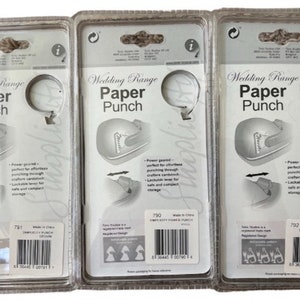 K&ouml;nnte beinhalten: Drei transparente Plastikverpackungen mit wei&szlig;em Hintergrund, jede mit einer silbernen Papierstanze mit der Aufschrift "Wedding Range Paper Punch". Die Verpackungen sind mit der Produktnummer 791, 790 und 792 gekennzeichnet.