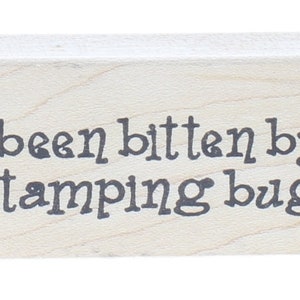 May include: A wooden rubber stamp with the text "I've been bitten by the stamping bug!" in black ink.