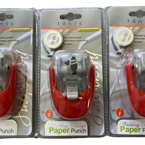 May include: Three red and silver paper punches with clear plastic tops. Each punch features a different wedding-themed design: a bride and groom, a bride and groom with a heart, and a bride with a veil. The packaging is silver with the word "Tonic" printed in black.
