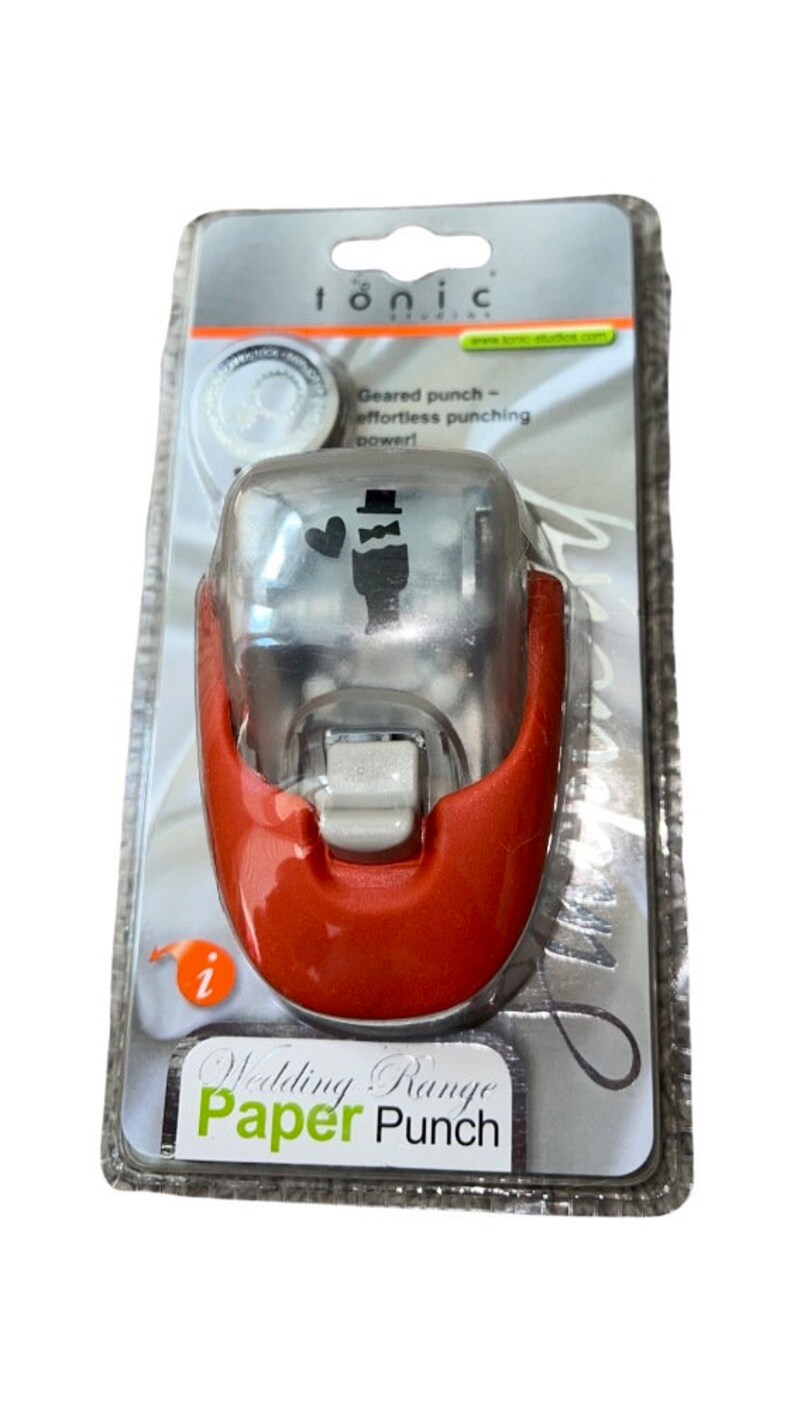 K&ouml;nnte beinhalten: Ein roter und silberner Papierstanzer mit Hochzeitsthema. Der Stanzer zeigt einen Br&auml;utigam mit Zylinder und einem Herzen. Die Verpackung lautet "Wedding Range Paper Punch".