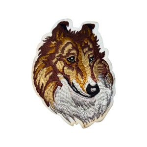 May include: Embroidered patch of a brown and white Collie dog's head. The dog is looking to the right and has a white patch on its chest.