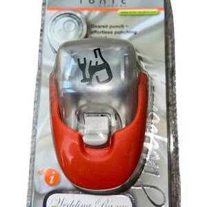 K&ouml;nnte beinhalten: Ein roter und silberner Papierstanzer mit einem Design aus Weinflasche und Gabel. Der Stanzer ist in einer durchsichtigen Plastikverpackung verpackt, auf der vorne der Text "Wedding Range Paper Punch" steht.