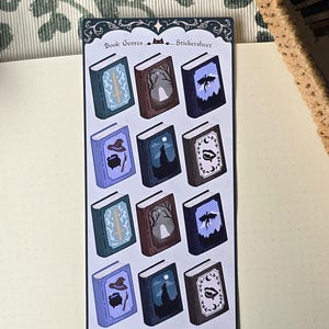 Op de afbeelding: Een rechthoekig stickervel met de titel Book Genres Stickersheet met twaalf individuele boekstickers gerangschikt in vier rijen. Elke boekomslag toont een unieke illustratie die een genre vertegenwoordigt, waaronder een zwaard, geest, draak, heksenhoed, ketel, toverstaf, wolf en vampiertanden.