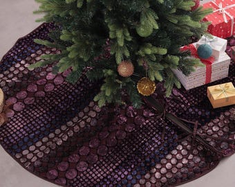 Puede incluir: Una falda de árbol de Navidad con un patrón de círculos morados oscuros y azules. La falda está debajo de un árbol de Navidad decorado con adornos y regalos envueltos. La falda tiene aproximadamente 122 cm de diámetro.