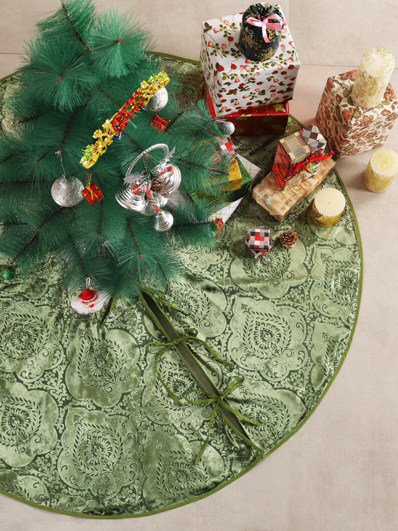 Puede incluir: Una falda de &aacute;rbol de Navidad verde con un estampado floral rodea un &aacute;rbol de Navidad artificial decorado. Los regalos envueltos en papel festivo y las velas est&aacute;n dispuestos alrededor del &aacute;rbol, creando una escena navide&ntilde;a.