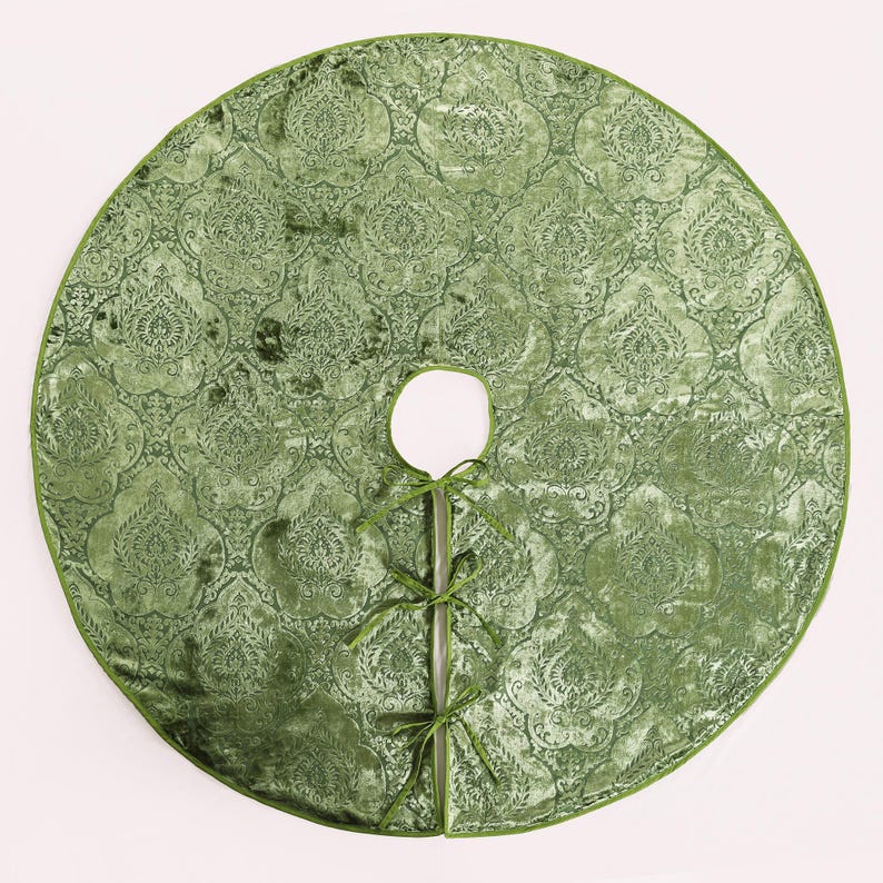 Puede incluir: Una falda redonda de &aacute;rbol de Navidad de terciopelo verde con un patr&oacute;n de damasco ornamentado. La falda tiene una abertura circular para el tronco del &aacute;rbol y est&aacute; bordeada con un borde verde a juego. Se adjuntan cintas verdes para sujetarla.