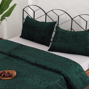 Pode incluir: Uma cama com um edredom texturizado verde escuro e duas almofadas a condizer. A cama tem uma cabeceira de metal preta. Uma bandeja de madeira com fruta está sobre o edredom. Uma planta em vaso está no fundo.