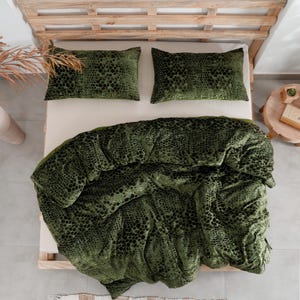 K&ouml;nnte beinhalten: Draufsicht auf ein Bett mit Holzrahmen, mit einer gr&uuml;nen Bettdecke und zwei passenden Kissenbez&uuml;gen. Die Bettw&auml;sche hat ein dunkles, gepunktetes Muster. Ein kleiner Nachttisch aus Holz und eine dekorative Vase sind sichtbar.