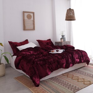 May include: A bed dressed with a deep burgundy velvet duvet cover and matching pillowcases. A white pillow is visible, along with a tray with cups and snacks. The bed is on a patterned rug.