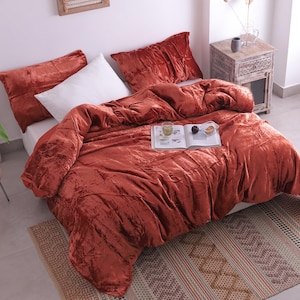 以下が含まれることがあります： 錆色のベルベットの掛け布団と、お揃いの枕カバーがセットされたベッド。白い枕が見えます。本とグラスの載ったトレイが掛け布団の上にあります。ベッドは模様入りのラグの上にあります。