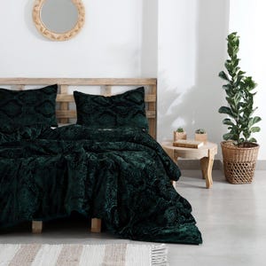 Könnte beinhalten: Ein Bett mit einer dunkelgrünen Samtdecke und passenden Kissenbezügen. Die Bettwäsche hat ein gemustertes Design. Der Bettrahmen ist aus hellem Holz. Ein runder Spiegel hängt an der Wand über dem Bett.