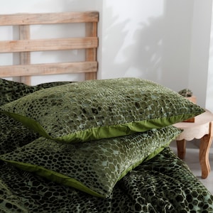 K&ouml;nnte beinhalten: Zwei gr&uuml;ne Zierkissen mit einem strukturierten Muster, gestapelt auf einer passenden Tagesdecke. Die Kissen haben einen einfarbigen gr&uuml;nen Rand. Die Tagesdecke und die Kissen liegen auf einem Bett mit einem h&ouml;lzernen Kopfteil.