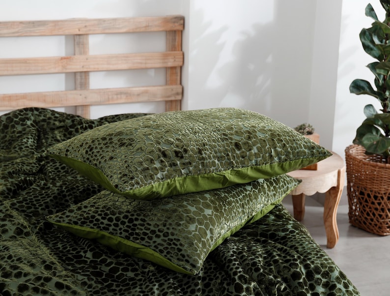 K&ouml;nnte beinhalten: Zwei gr&uuml;ne Zierkissen mit einem strukturierten Muster, gestapelt auf einer passenden Tagesdecke. Die Kissen haben einen einfarbigen gr&uuml;nen Rand. Die Tagesdecke und die Kissen liegen auf einem Bett mit einem h&ouml;lzernen Kopfteil.