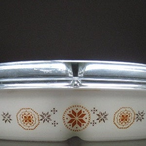 Puede incluir: Plato para hornear ovalado blanco con tapa plateada. El plato tiene un patrón floral marrón y naranja.