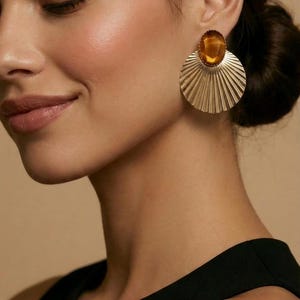 May include: Gold-coloured earrings featuring a large, amber-coloured stone centre and a fan-shaped design. These earrings are a statement piece, adding a touch of glamour. A bold accessory.