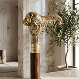 Può includere: Bastone decorativo con manico a forma di testa di leone dorata. Il manico è dettagliato con criniera e lineamenti del viso. L'asta è in legno marrone scuro, con dettagli dorati nella parte superiore.