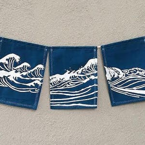 May include: A banner with five navy blue rectangular flags. Each flag features a white wave design. The flags are connected by a thin white string. The banner is hanging against a light gray background.