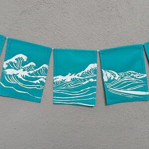 May include: A teal banner with five rectangular flags, each displaying a white wave design. The flags are strung together with a white cord, creating a decorative garland. The background is a solid gray.