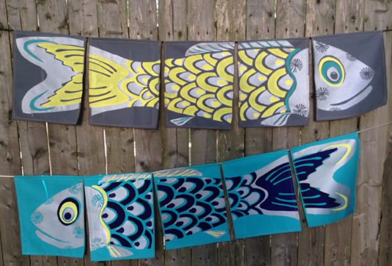 Puede incluir: Una hilera de siete banderas de tela con forma de pez, de colores vivos, colgadas de una valla de madera. Las banderas est&aacute;n hechas de tela gris claro con un dise&ntilde;o de pez azul y amarillo. Los peces tienen escamas y aletas, y algunos tienen ojos. Las banderas son una decoraci&oacute;n divertida y festiva para cualquier ocasi&oacute;n.