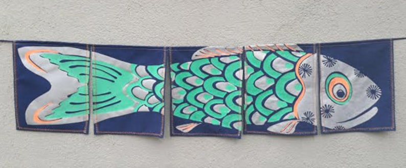 Puede incluir: Una pancarta de tela con forma de pez colorida con fondo azul y detalles verdes y naranjas. La pancarta est&aacute; dividida en cinco secciones, cada una con una parte diferente del dise&ntilde;o del pez.