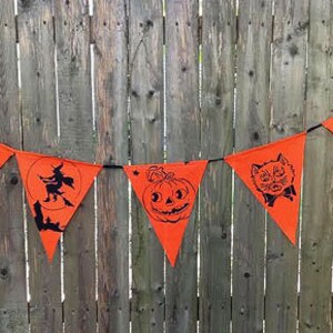 Puede incluir: Una pancarta de Halloween naranja y negra con varias im&aacute;genes, incluyendo una bruja, un gato, una calabaza y una casa encantada. La pancarta est&aacute; colgada en una valla de madera.
