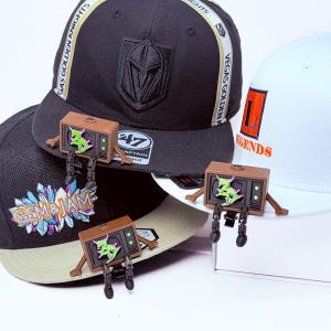 Three Zeds Dead articulated TV buddy each sitting on a white, black, beige  brim with legs dangling