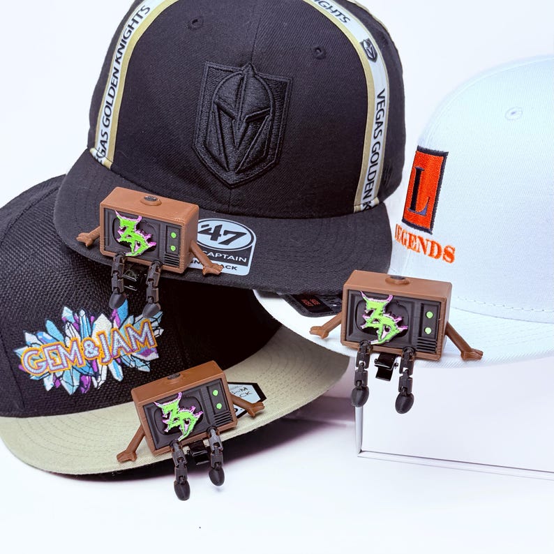Three Zeds Dead articulated TV buddy each sitting on a white, black, beige  brim with legs dangling