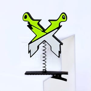 May include: A hair accessory featuring a crossed pair of stylized daggers in neon green and silver, attached to a black metal alligator clip by a thin, flexible black coil spring. The design has sharp, jagged edges and a bold, high-contrast aesthetic.