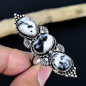 Può includere: Un anello d'argento con tre pietre a motivi bianchi e neri. L'anello ha un design ornato con un'incastonatura dettagliata attorno a ogni pietra. Le pietre sono a forma di goccia e ovali.
