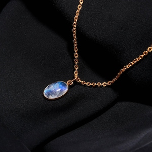 May include: A gold-colored chain necklace with an oval pendant. The pendant features a blue and white gemstone. The necklace is displayed on a black background.