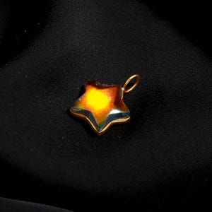 May include: A star-shaped pendant with a gold-coloured frame and a colourful, iridescent centre. The pendant has a loop at the top for a chain. The colours transition from yellow to orange and blue.