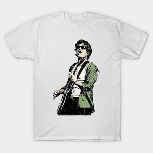 Könnte beinhalten: Weißes T-Shirt mit einer stilisierten Illustration in Schwarz, Weiß und Grün einer Person, die Gitarre spielt. Die Person trägt eine Sonnenbrille und eine grüne Jacke über einem weißen Tanktop.