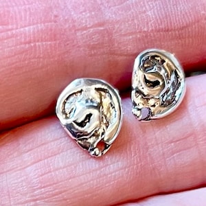 May include: A pair of silver earrings with a unique, abstract design. The earrings are small and delicate, and they have a textured surface.