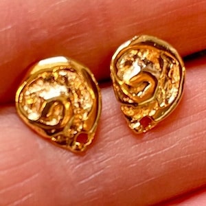 May include: A pair of gold-toned earrings with a textured, swirl design. The earrings are small and delicate.
