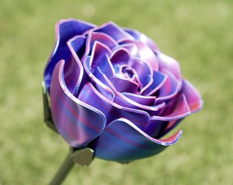 Può includere: Una scultura di rosa in metallo realizzata a mano con petali a strati nei toni del viola, blu e rosa. Lo stelo è di colore verde tenue e lo sfondo è verde sfocato. Questo pezzo decorativo è un oggetto d'arte floreale unico.