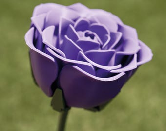 Può includere: Primo piano di una rosa viola con più petali. La rosa è in piena fioritura e ha uno stelo verde scuro. Lo sfondo è verde sfocato.
