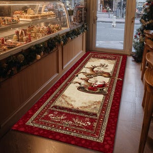 Op de afbeelding: Een rechthoekig kersttapijt met een rode rand en een cr&egrave;mekleurig middenstuk. Het middenstuk toont de kerstman in een slee getrokken door rendieren. Het tapijt ligt voor een deuropening, met een bakkerijvitrine zichtbaar.