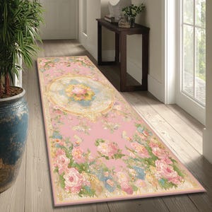 Op de afbeelding: Een rechthoekig roze loper met een bloemenpatroon. Het tapijt heeft een centraal medaillon met een bloemenontwerp in geel, blauw en roze, omgeven door een gouden rand. De randen zijn versierd met roze rozen, vlinders en andere bloemen.