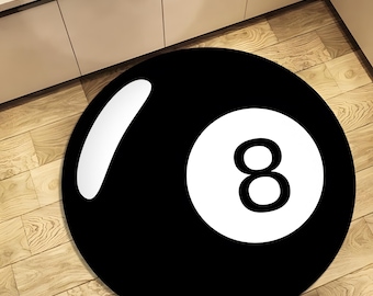 May include: A round black rug with a white number eight and a white curved stripe, resembling a pool ball. The rug is on a light brown wooden floor.